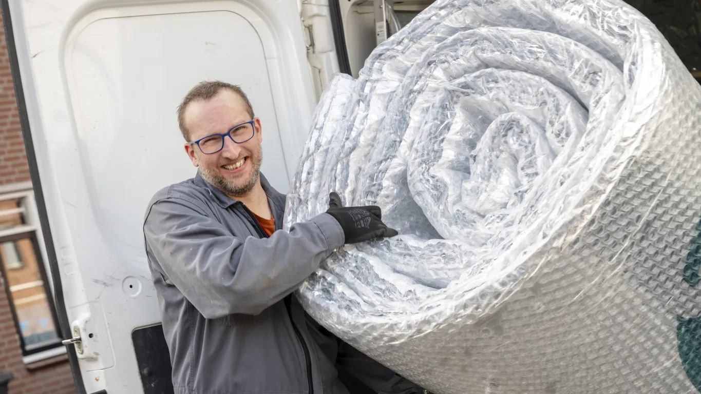 Man met lach op zijn gezicht laadt pif-isolatie uit achterkant van een witte bus