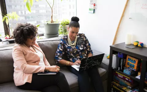 Twee vrouwen zijn samen in gesprek op de bank. Eentje heeft een laptop.