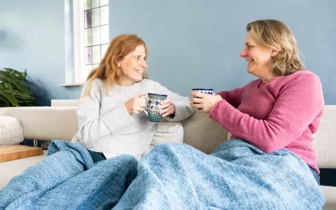 Twee mensen op de bank. Drinken een kop thee en zitten onder een deken.