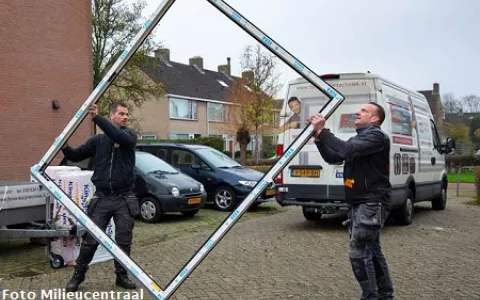 Twee mannen tillen een nieuw kunststof kozijn richting een woning die verbouwd wordt