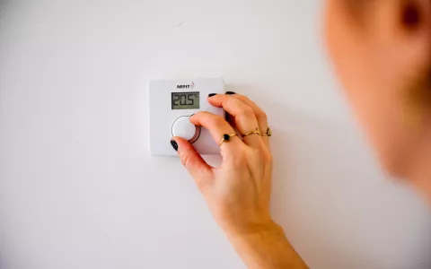 Een persoon draait de thermostaat in huis op 20 graden