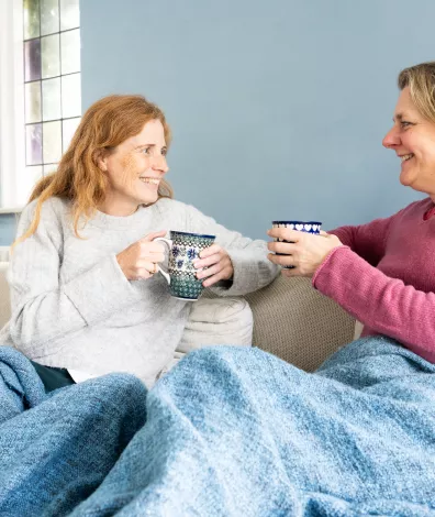 Twee mensen op de bank. Drinken een kop thee en zitten onder een deken.
