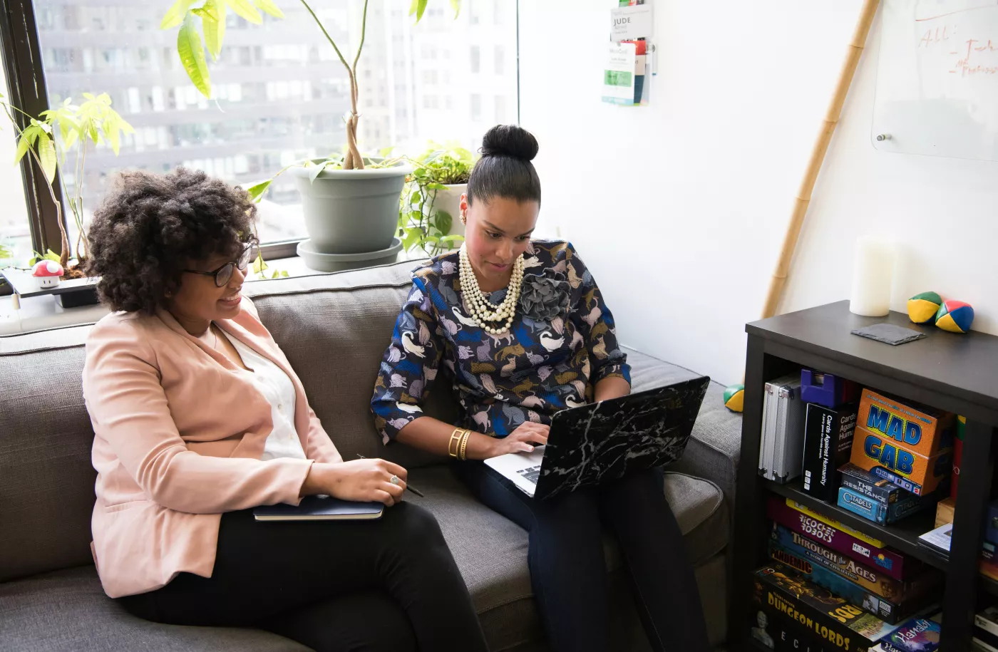 Twee vrouwen zijn samen in gesprek op de bank. Eentje heeft een laptop.