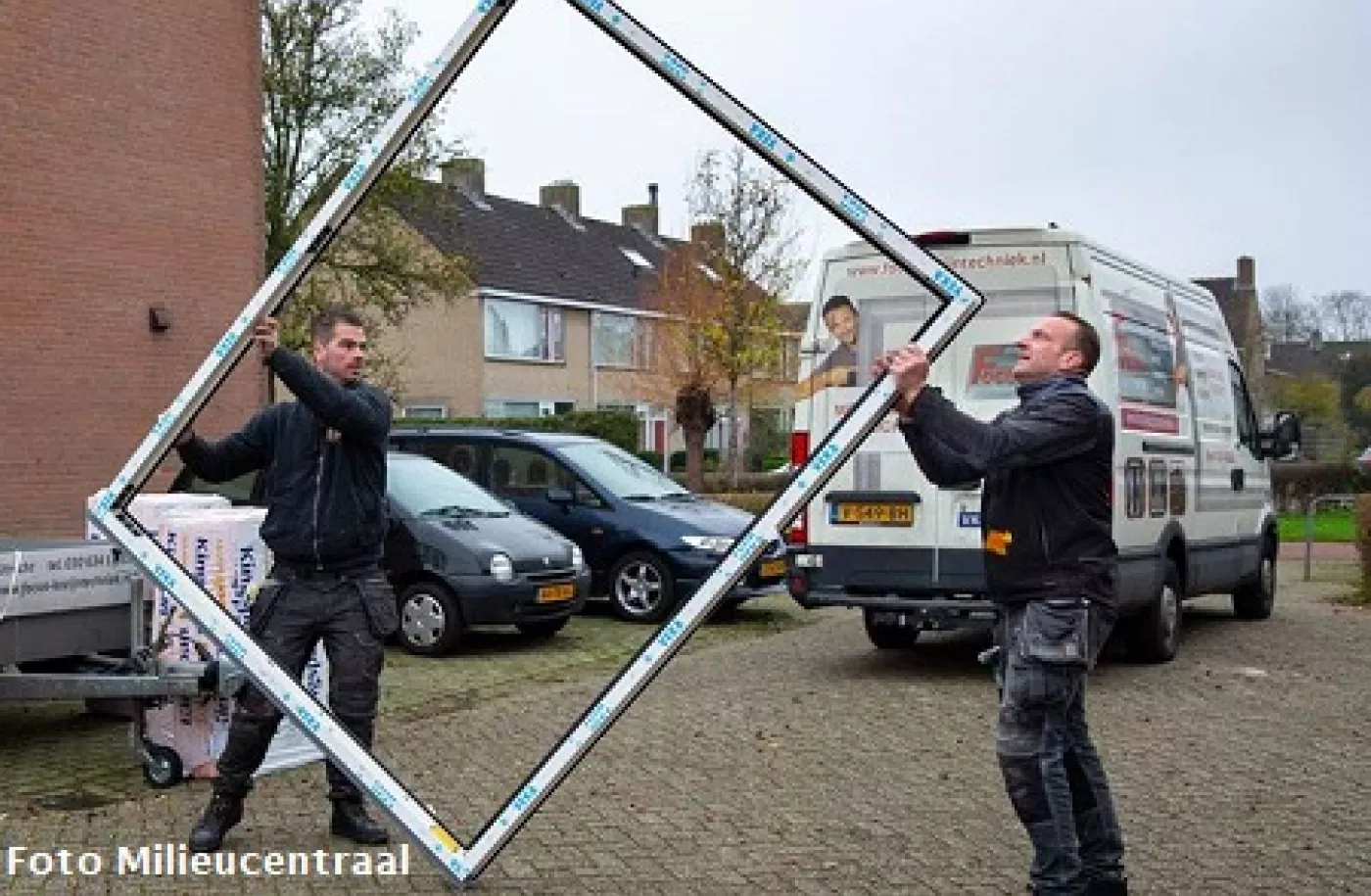 Twee mannen tillen een nieuw kunststof kozijn richting een woning die verbouwd wordt
