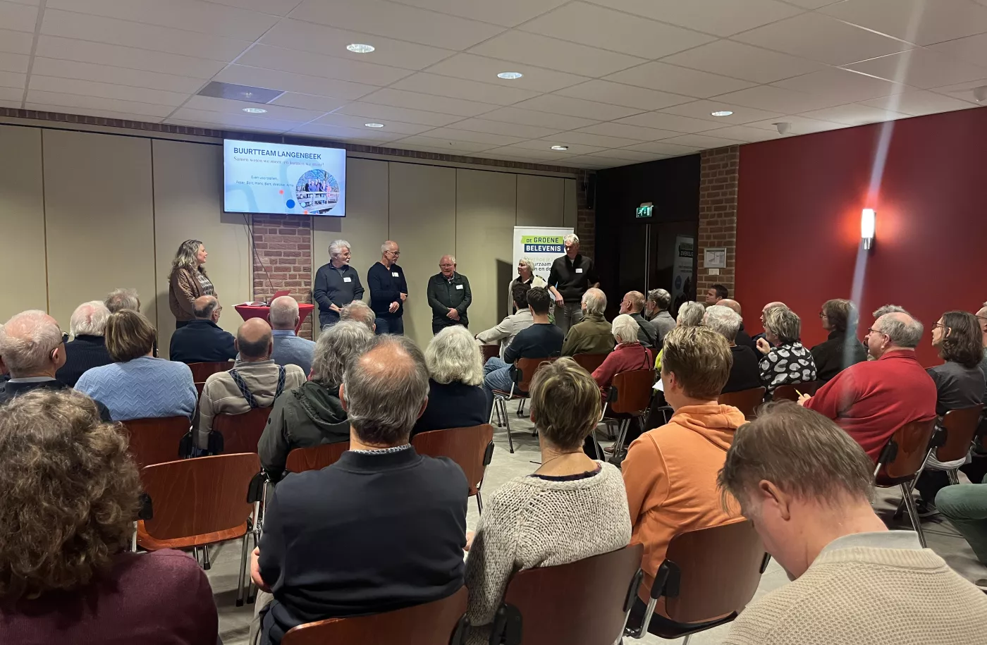 Een zaal vol mensen in De Koningshof te Leusden die luisteren naar een presentatie van het buurtteam van de buurt Langenbeek