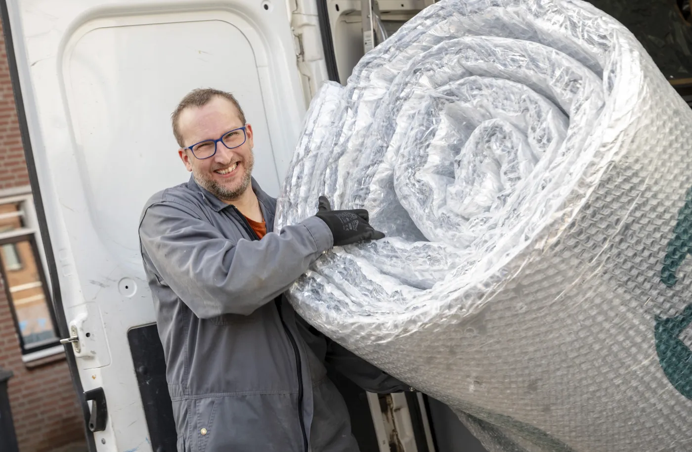 Man met lach op zijn gezicht laadt pif-isolatie uit achterkant van een witte bus