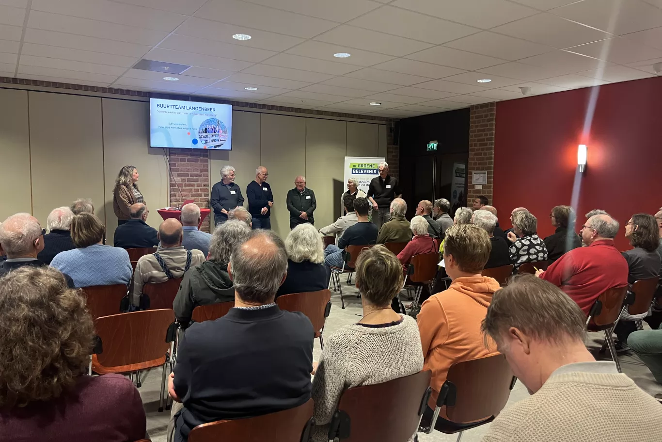Een zaal vol mensen in De Koningshof te Leusden die luisteren naar een presentatie van het buurtteam van de buurt Langenbeek